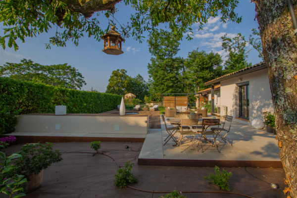 Aménagement de jardin contemporain avec terrasse en dalles, coin repas, et plateforme en bois surélevée pour la détente.