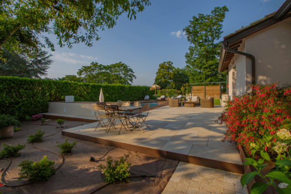 Aménagement paysager moderne: grande terrasse en dalles de pierre avec mobilier extérieur, bordures métalliques et jardin luxuriant.