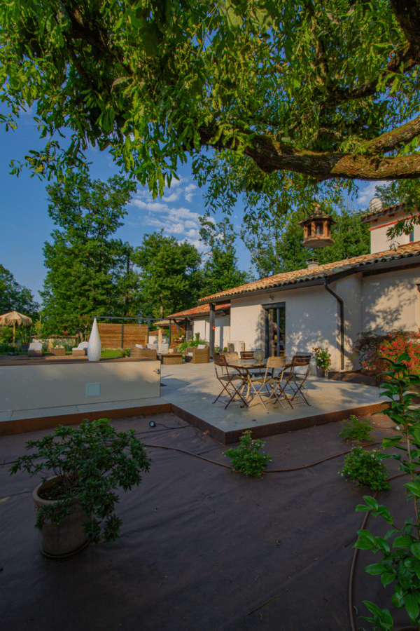 Vaste terrasse moderne et jardin d'une maison blanche. Mobilier extérieur élégant et coin bistrot sous l'ombre des grands arbres.