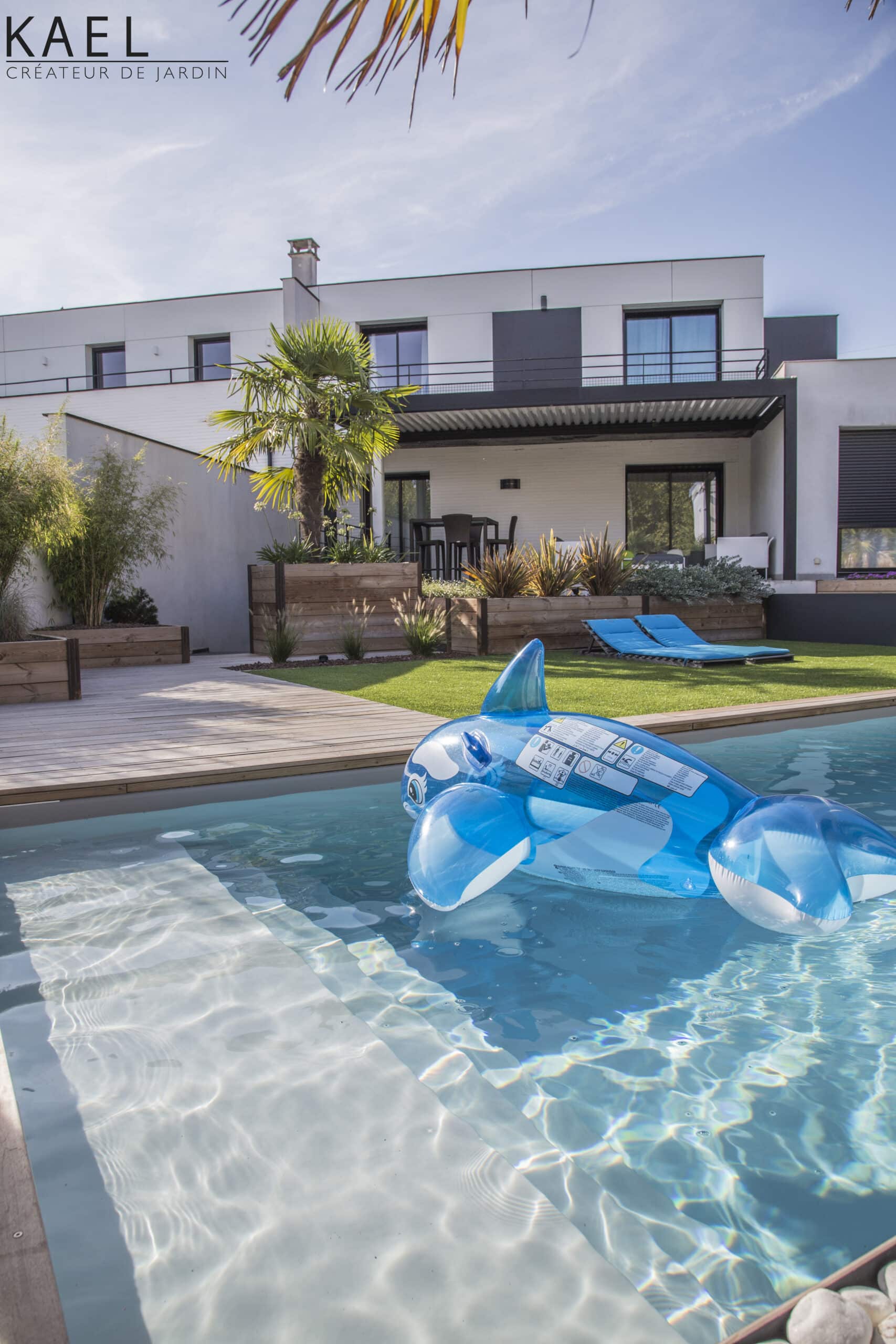 Aménagement de jardin Kael : piscine avec baleine gonflable, terrasse en bois et maison moderne blanche.