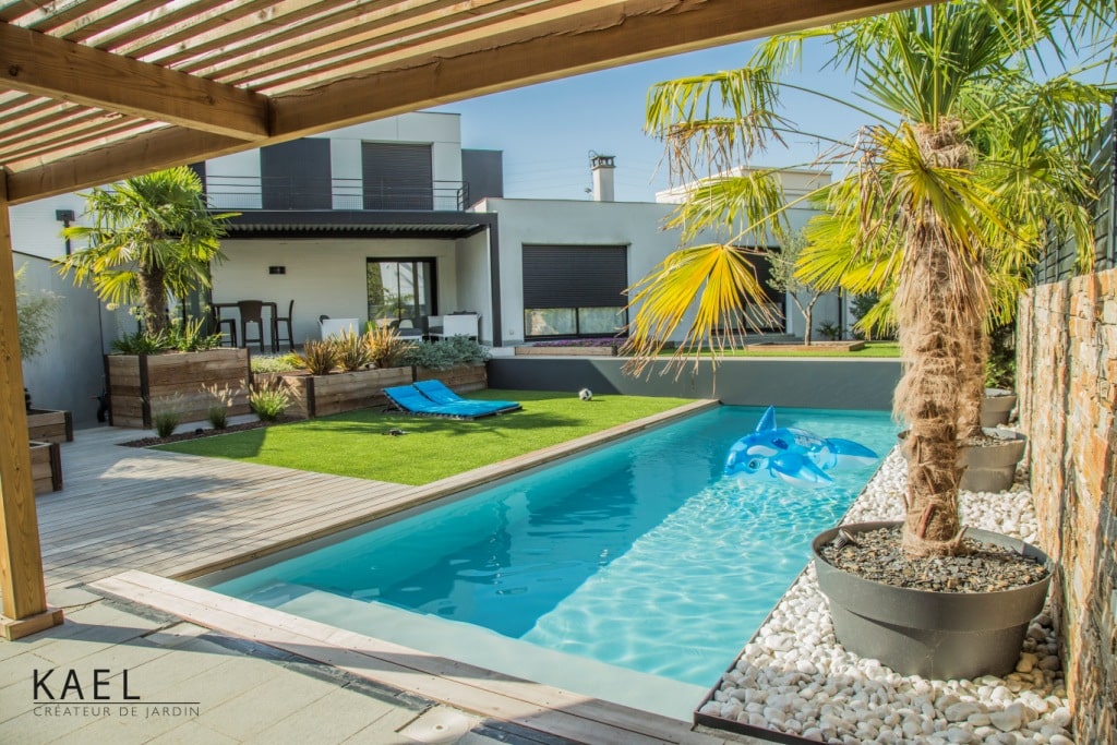 Jardin moderne avec piscine rectangulaire, terrasse en bois et palmiers par KAEL Créateur de jardin.