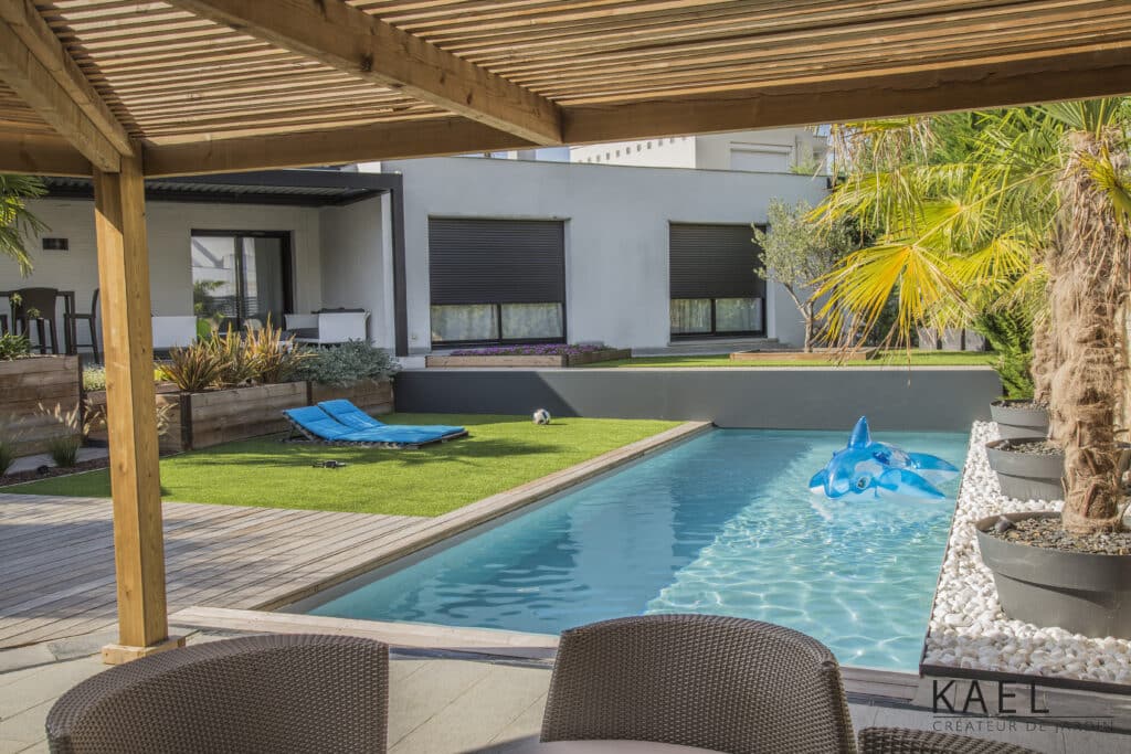 Aménagement jardin KAEL : piscine, pergola en bois, transats bleus et gazon. Espace de détente extérieur moderne.