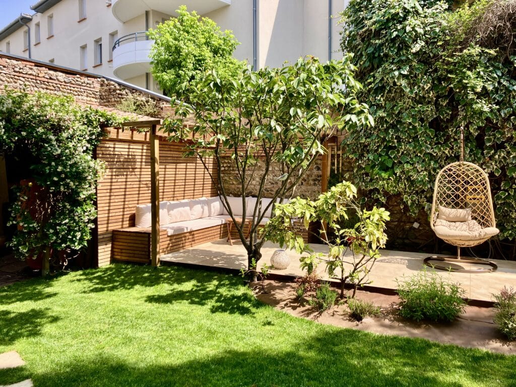 Jardin moderne avec pergola en bois, banquette confortable et fauteuil suspendu sur une pelouse ensoleillée.