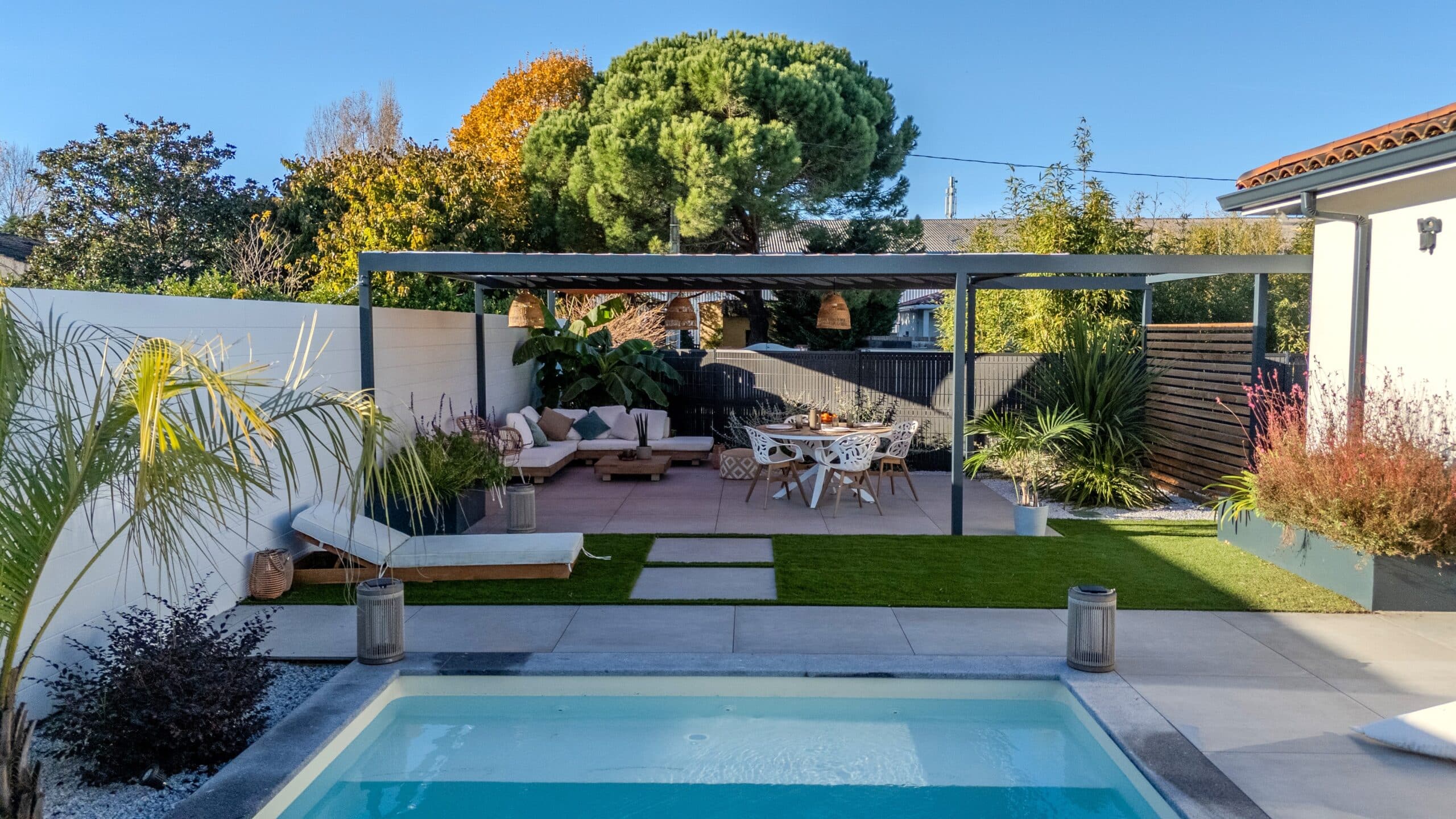 Aménagement extérieur moderne avec piscine, pergola grise, salon de jardin et coin repas sous un soleil radieux.