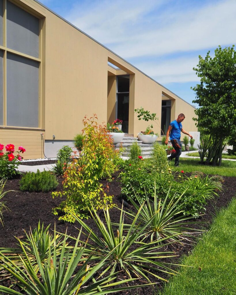 Paysagiste entretenant un jardin moderne avec yucca et arbustes devant une villa contemporaine beige.