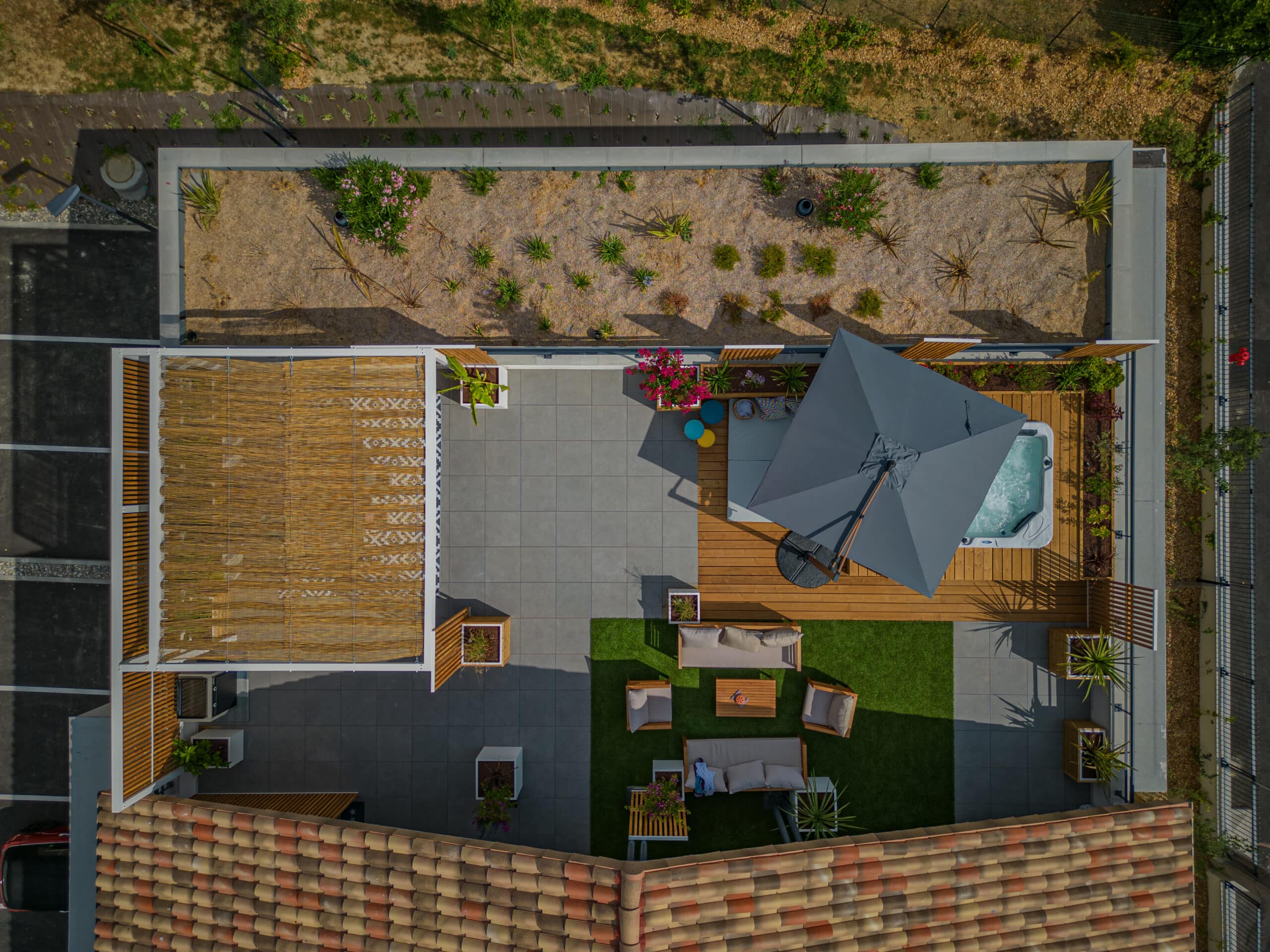 Terrasse moderne avec jacuzzi, pergola en bambou, salon de jardin et parasol gris vus du ciel.
