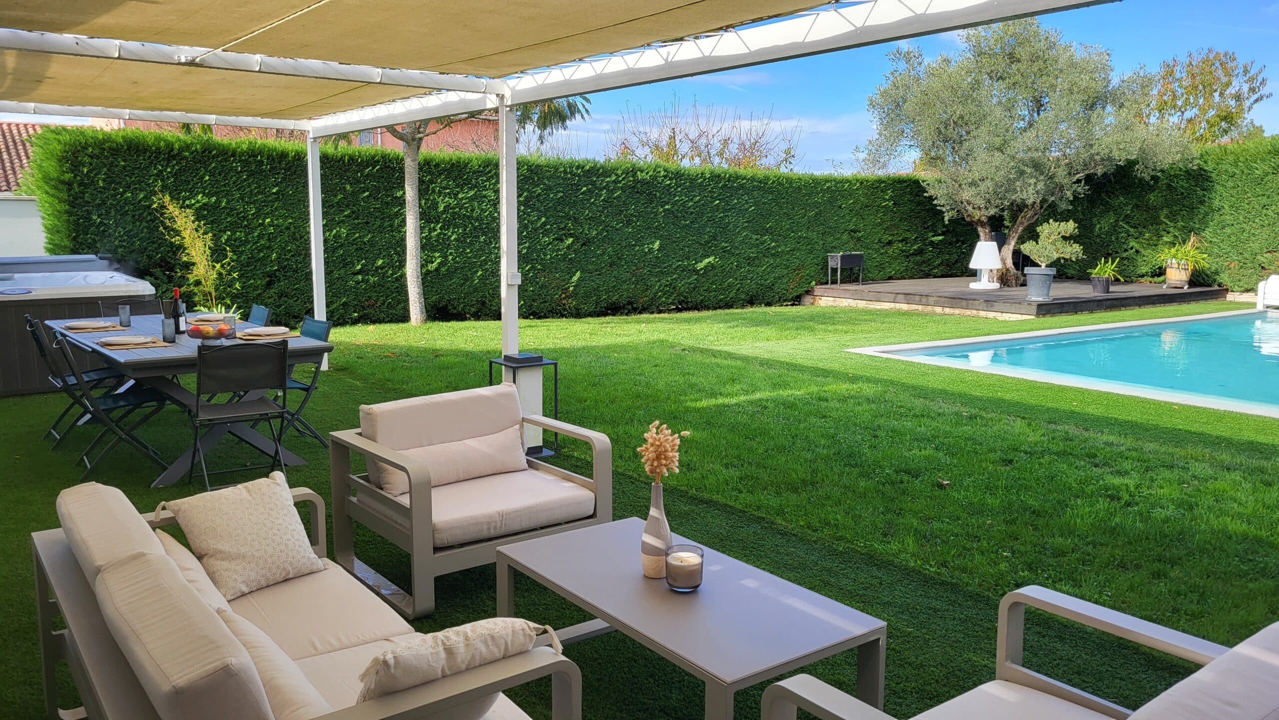 Terrasse avec salon de jardin, coin repas sous pergola et piscine dans un jardin arboré.