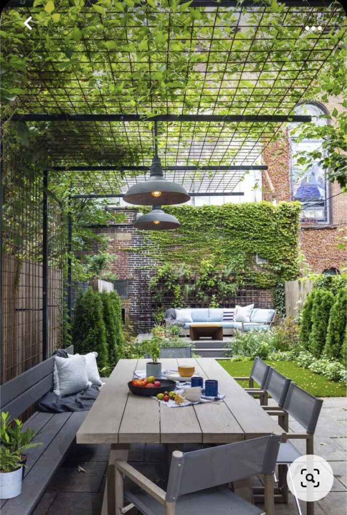 Terrasse urbaine avec table en bois sous une pergola végétalisée et salon de jardin moderne entouré de verdure.