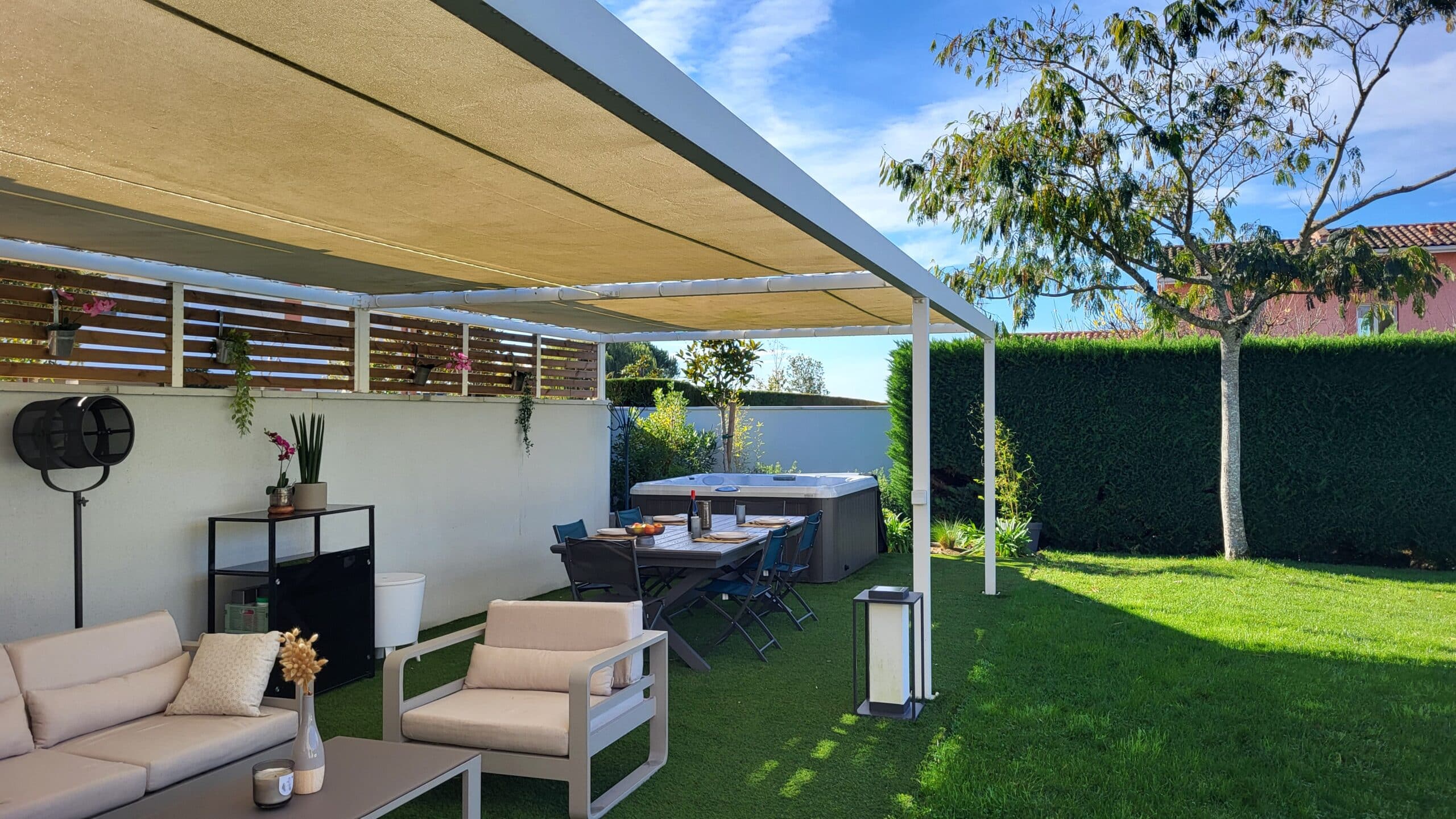 Terrasse avec pergola, salon de jardin moderne, spa extérieur et coin repas dans un jardin ensoleillé avec pelouse.