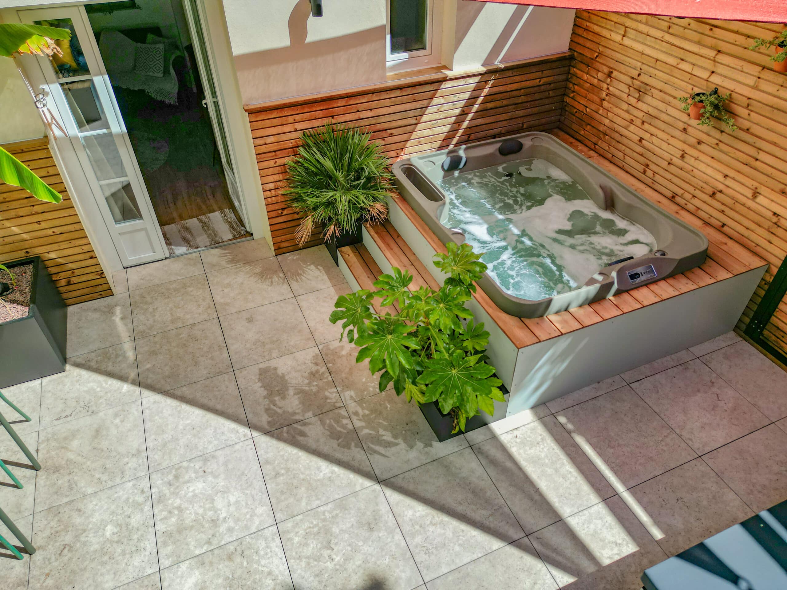 Terrasse moderne avec spa bouillonnant, habillage bois, plantes et carrelage clair pour un espace détente extérieur.