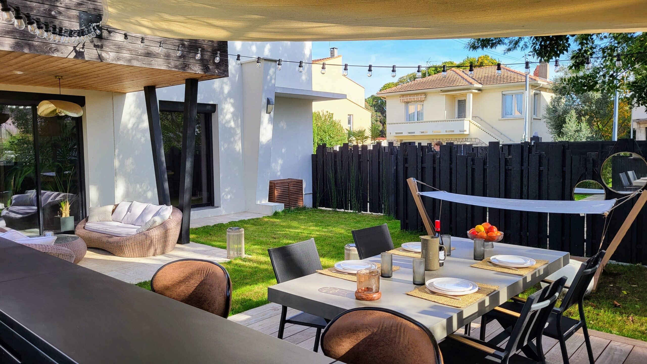 Terrasse moderne avec table dressée, salon de jardin et voile d'ombrage dans un cadre extérieur contemporain.