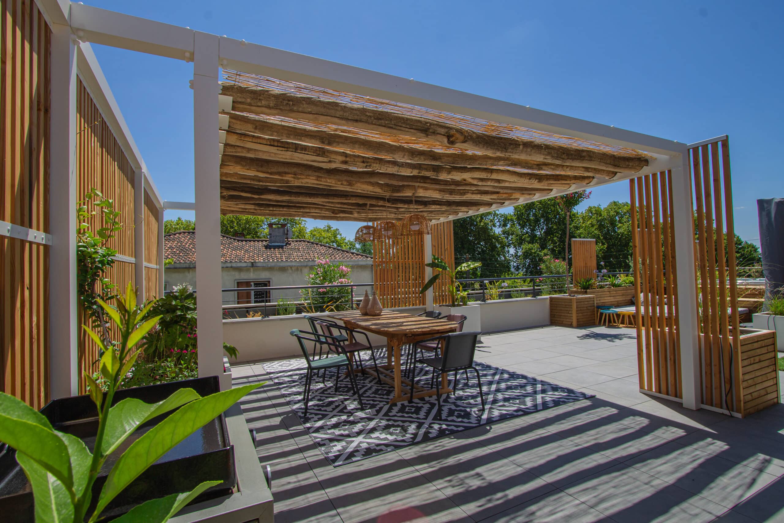 Terrasse de toit moderne avec pergola en bois, table à manger, chaises et tapis géométrique sous un ciel bleu.